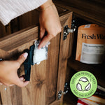 Hands inserting a clear sachet of odor-removing beads into a black Fresh Wave pod inside a wooden cabinet with product pouch visible