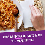 Lifestyle shot of a hand next to a folded white napkin beside a plate of spaghetti and meatballs