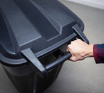 Hand gripping the rear handle of a black plastic wheeled trash can, close-up of lid and handle area.