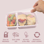 Hand lifting clear lid off a blush pink two-compartment container filled with vegetables and wraps, icons for features below.