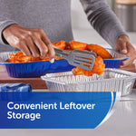 Hand using tongs to place a chicken wing into a small aluminum foil tray with larger blue pan in background