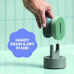 Hand placing the Brite scrubber head above its drain-and-dry stand on a mint-tiled countertop with a feature badge