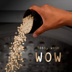 Hand pouring beige scent beads from a black scoop into a washing machine drum with 'Toss, Wash WOW' text