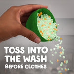 Hand pouring green and orange Gain scent beads from a green scoop with text instructing toss into the wash before clothes