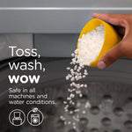 Hand pouring white scent beads from a yellow scoop into a washing machine with text 'Toss, wash, wow'.