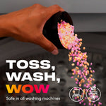 Hand pouring pink and orange Unstopables scent beads from a black scoop into a washing machine with 'Toss, Wash, Wow' text