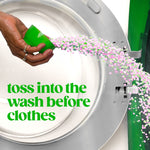 Hand tipping green cap to pour pink and green scent booster beads into an open washing machine