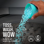 Hand pouring teal laundry scent beads from a measuring cup into a washing machine drum with usage text