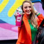 Person holding a can of Citrus Magic Dragonfruit car spray toward the camera with colorful mural background