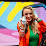Close-up of a hand presenting a Citrus Magic Georgia Peach spray can with colorful mural background