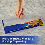 Hand pulling a pre-cut parchment sheet from a Reynolds Kitchens pop-up parchment box on a marble surface.