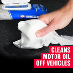 Hand pulling a white STP oil wipe from a blue package on a dark work surface, with text overlay that reads cleans motor oil off vehicles
