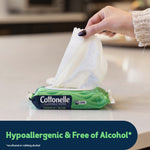 Hand pulling a wipe from a green Cottonelle GentlePlus flushable wipes pack on a countertop with flip-top lid open