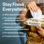 Hand pulling a wipe from an open Honest Flushable Wipes pack with checklist of uses and bathroom setting in background