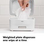 Hand pulling a single wet wipe from an open white OXO dispenser with lid up