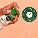 Hand pressing the pump of a Miracle-Gro Indoor Plant Food bottle with liquid dispensing and a 'Feeds Instantly' icon beside it.