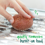 Hand holding a copper-coated scouring pad scrubbing a metal surface, with text indicating it removes burnt-on food