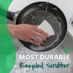 Hand using a white Greener Clean sponge to scrub a nonstick frying pan under running water at a sink