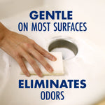 Close-up lifestyle photo of a hand scrubbing a sink drain with a sponge and baking soda, overlaid with text “GENTLE ON MOST SURFACES” and “ELIMINATES ODORS.”