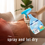 Hand holding Febreze Fabric spray and misting a rust-colored decorative pillow on a couch
