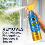 Hand spraying Pledge multisurface cleaner toward a window, can labeled fresh citrus scent
