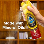 Hand spraying a yellow Pledge wood oil can with mist visible and overlay text stating made with mineral oils.