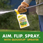 Hand holding a Spectracide Weed & Feed bottle attached to a hose nozzle spraying liquid over a lawn
