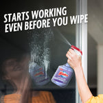 Hand spraying Windex ammonia-free bottle onto a glass surface with visible spray and product reflection, statement text above