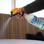 Hand holding and spraying a Zep professional bottle with visible fine mist and a yellow-blue trigger nozzle in use.