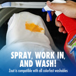 Hand holding a red Zout spray over a white garment with an orange stain and text 'Spray, work in, and wash!' at bottom