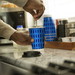 Hand stirring a beverage in a blue-patterned Chinet Comfort paper cup on a kitchen counter