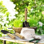 Garden scene with hand trowel, small rake, spray bottle and sun hat on table beside a woven basket