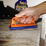 Hand pressing an orange-handled scrubber across metal grill grates with a blurred Citrusafe bottle behind it.