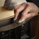 Close-up of a hand using a steel wool pad to sand or clean a metal edge with loose fibers visible
