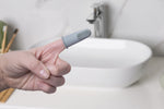 Close-up lifestyle image of a hand wearing a gray bizzu silicone finger toothbrush over a bathroom sink.