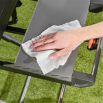 A hand using a white textured pre-moistened cloth to wipe a gray grill side shelf, showing cleaning action.