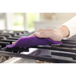 Hand holding a purple abrasive scrub pad and wiping a stovetop grate in a kitchen setting