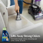 Handheld upholstery tool cleaning a light-colored couch with BISSELL upright cleaner visible in background and product inset