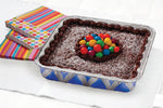 Baked chocolate square cake served in a Handi-Foil blue geometric printed aluminum pan next to colorful napkins