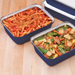 Two blue Handi-foil oblong meal prep pans filled with pasta and mixed vegetables on a wooden surface