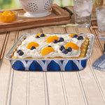 Filled square foil pan with cream-topped dessert garnished with mandarin slices and blueberries in a Handi-Foil blue printed pan