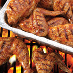 Close-up of grilled chicken wings in a Handi-Foil disposable aluminum pan over flames on a grill