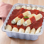 Close-up of an aluminum foil pan filled with stuffed pasta topped with red tomato sauce on a wooden surface
