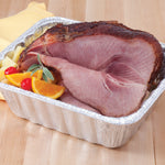 Cooked ham and fruit arranged inside a Handi-Foil disposable aluminum pan on a wooden surface