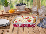 Decorated cake in a red-printed Handi-foil square aluminum pan on a wooden table set with plates and glasses outdoors