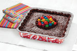 Baked chocolate cake presented in a red printed Handi-foil square aluminum pan on a table beside colorful napkins