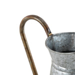 Detail view of a curved brown metal handle welded to the rim of a galvanized pitcher