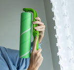 Hands holding a green Evercare lint roller vertically near a window while adjusting the handle