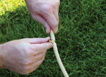 Close-up of hands attaching a small brass mist nozzle into tan misting tubing on grass surface.