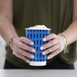 Person holding a blue-patterned Chinet Comfort cup topped with foam against neutral background